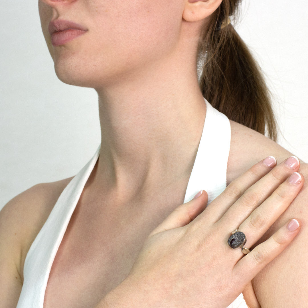 Woman wearing a silver ring with a rough red stone on a plain background