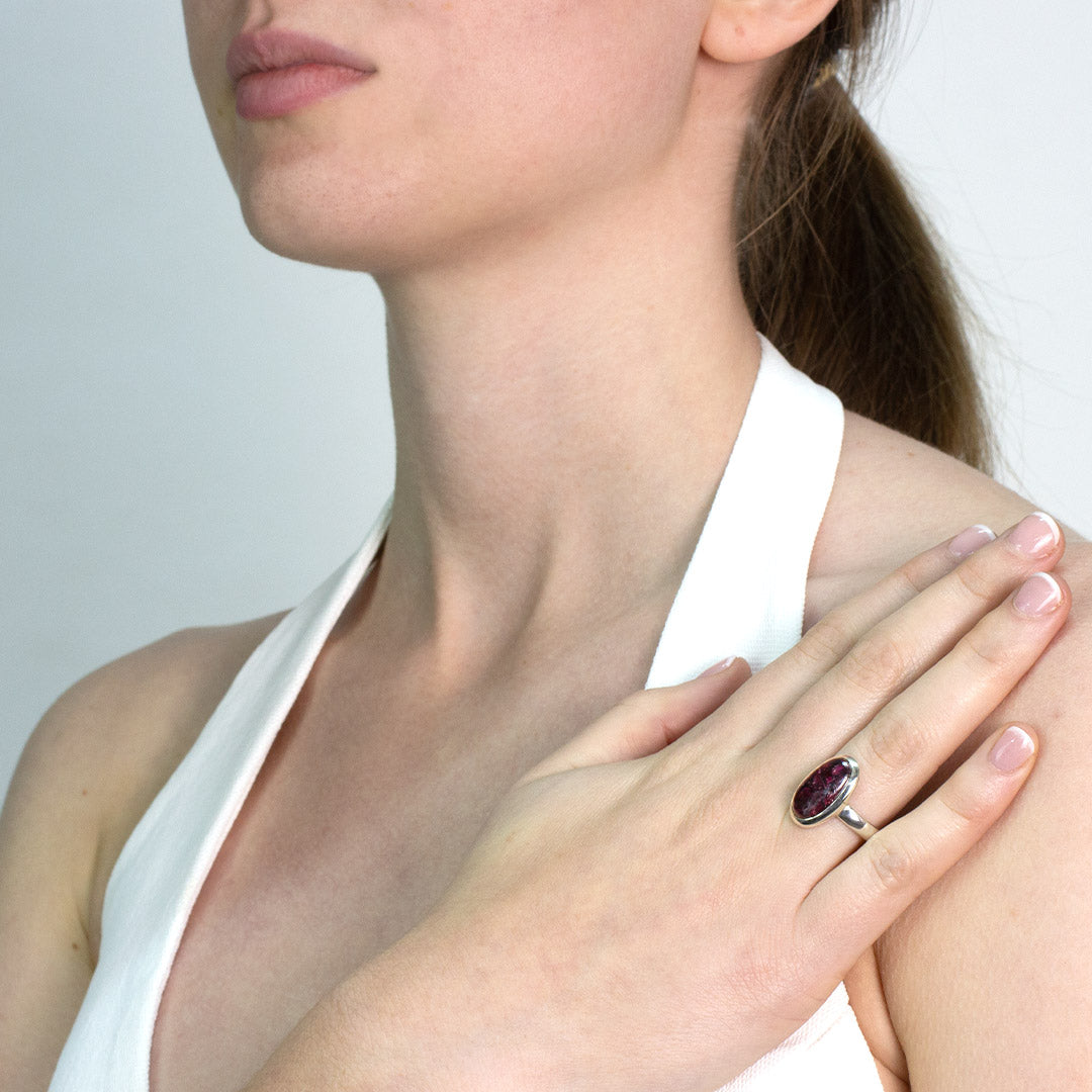 Woman wearing a silver ring with a dark pink gemstone on a plain background