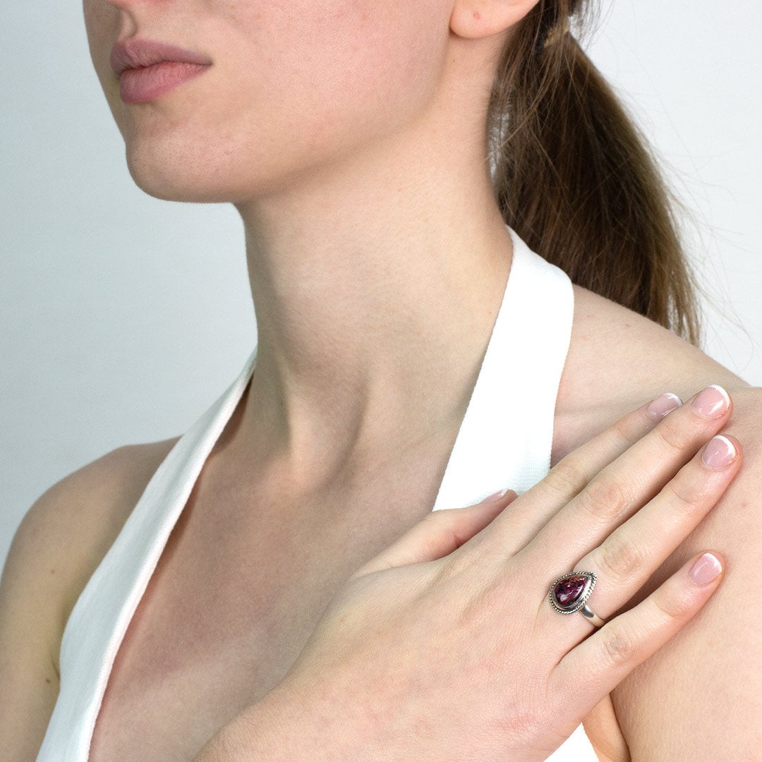 Woman wearing a silver ring with a dark pink gemstone on a plain background