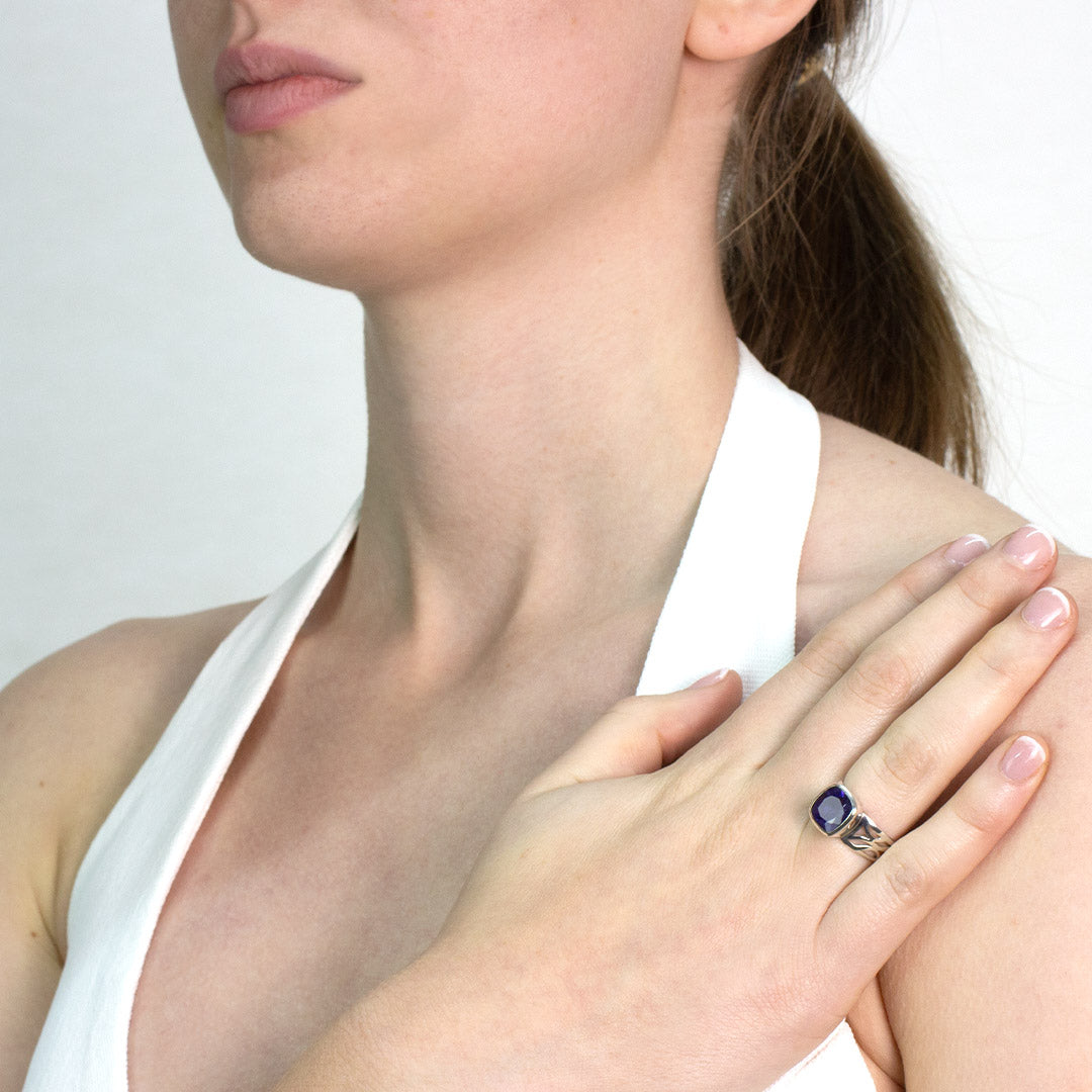 Woman wearing a silver ring with a violet gemstone on a plain background
