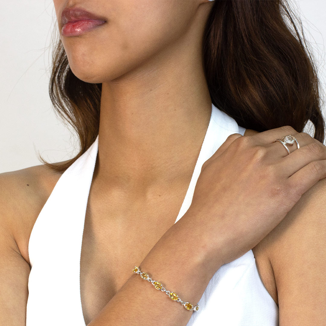 Woman wearing a silver bracelet with yellow gemstones on a plain background