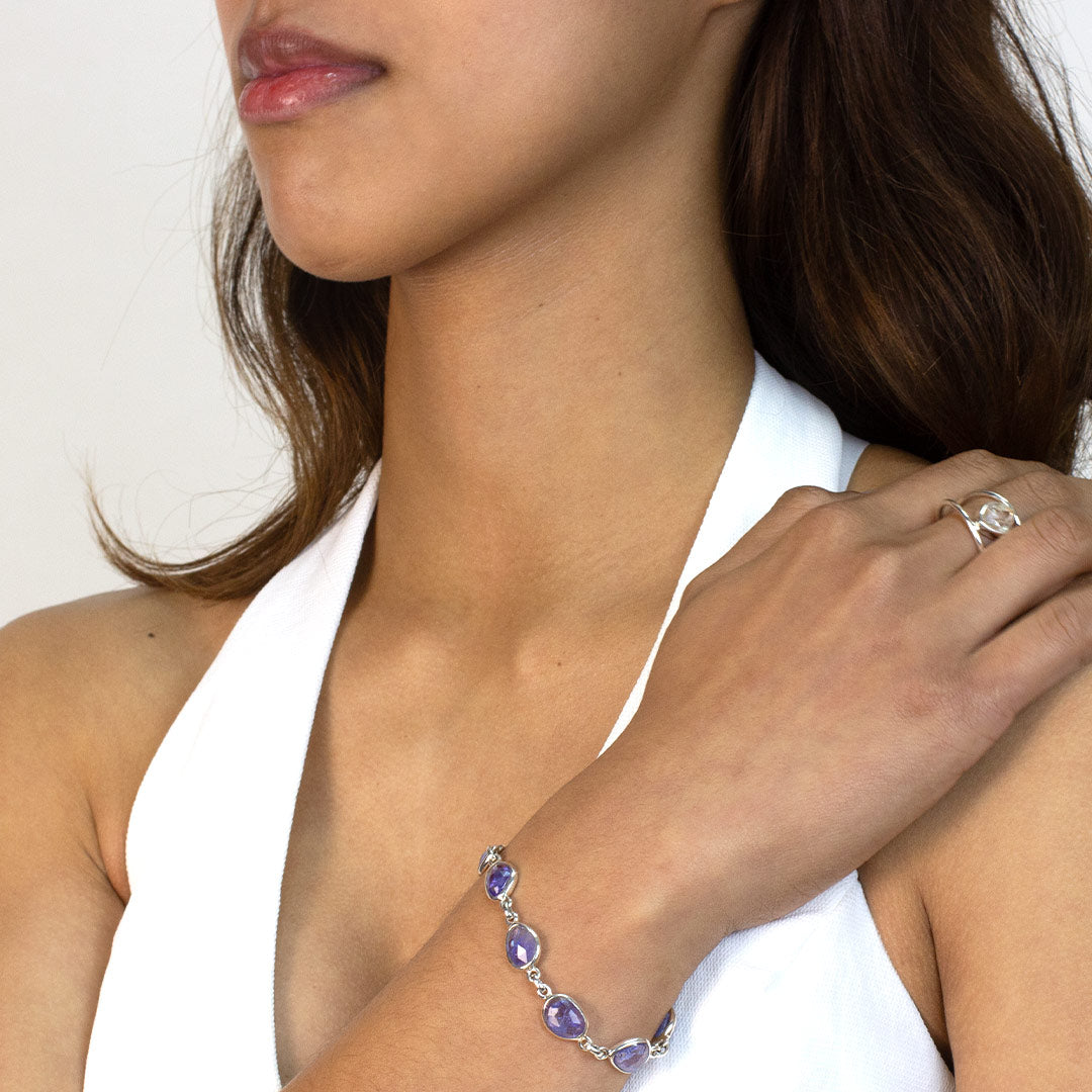 Woman wearing a silver bracelet with blue gemstones on a plain background