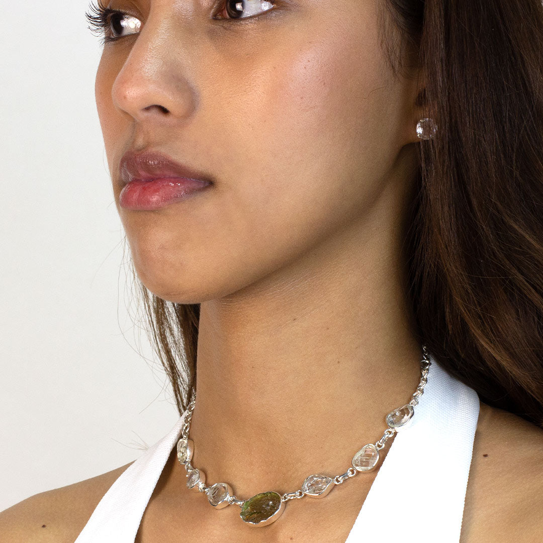 Woman wearing a silver necklace with green and clear gemstones on a plain background