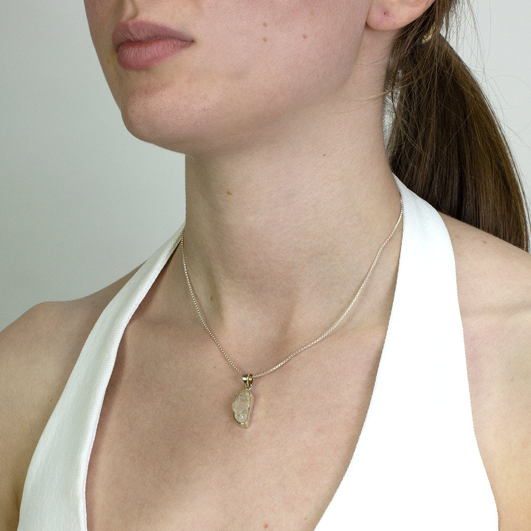 Woman wearing a silver necklace with a clear gemstone on a plain background