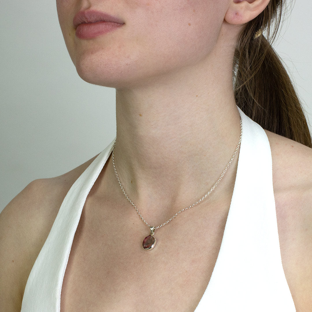 Woman wearing a necklace with a pendant featuring a pink and green stone on a plain background