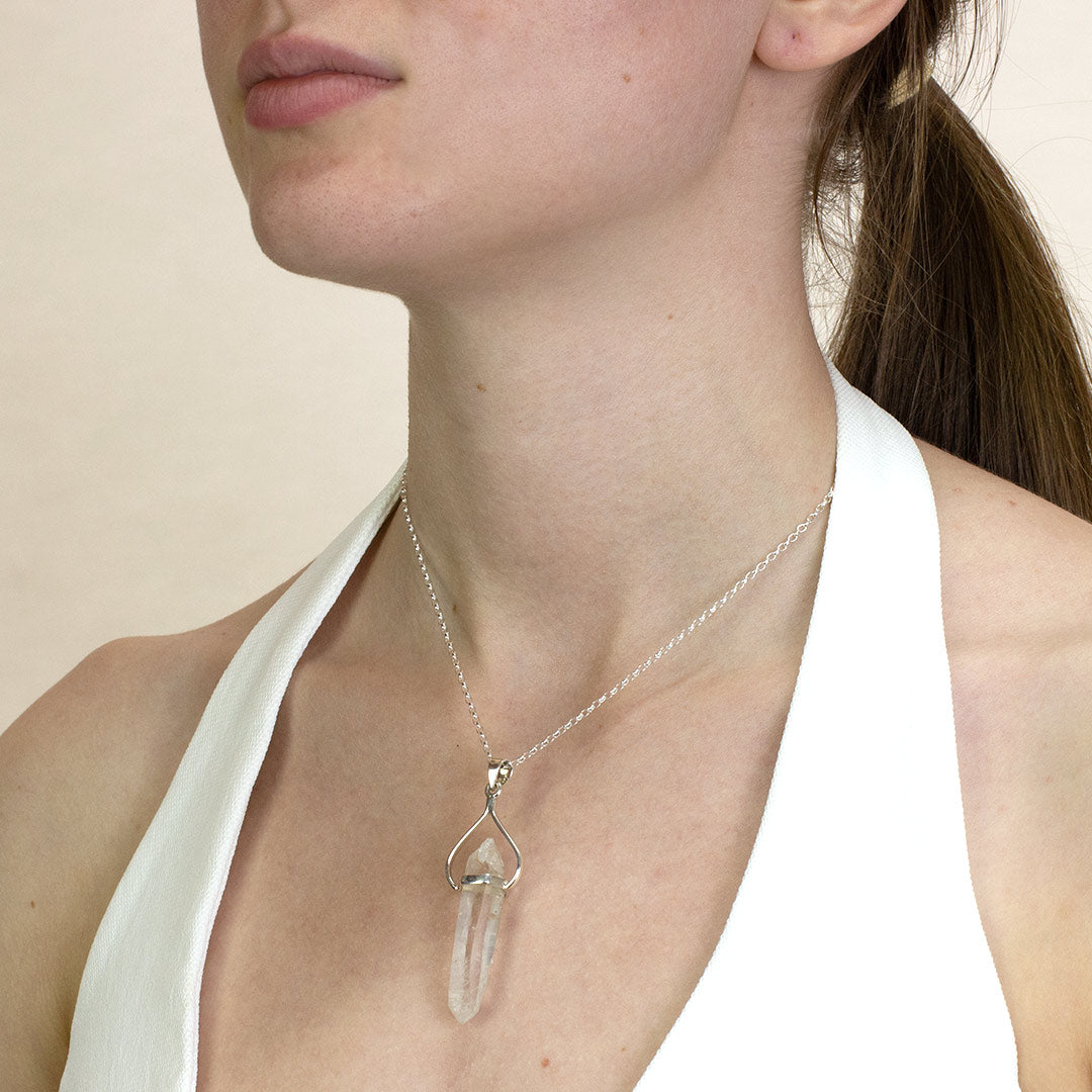Person wearing a silver necklace with clear gemstone on a plain background