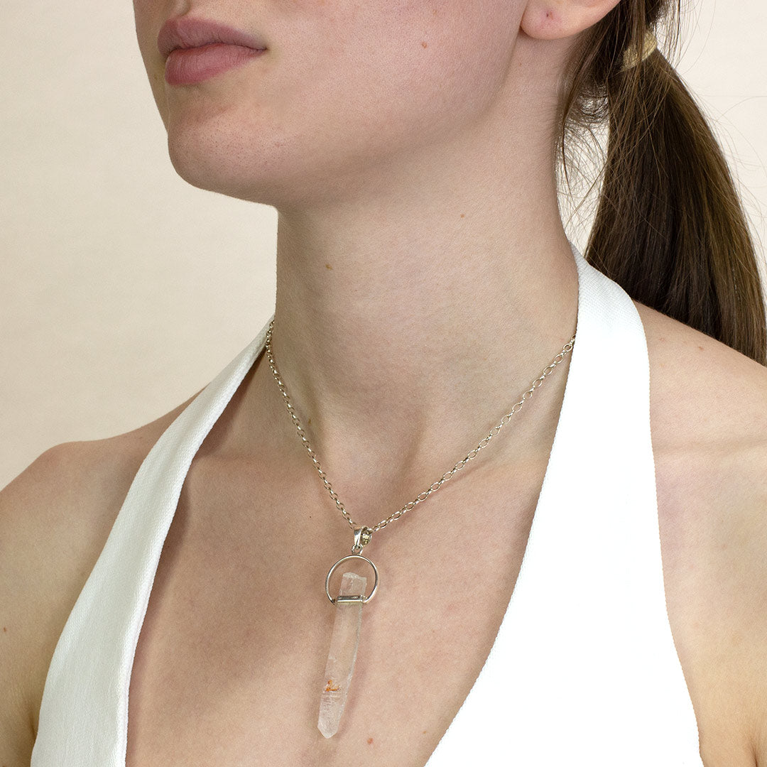 Person wearing a silver necklace with a clear stone on a plain background
