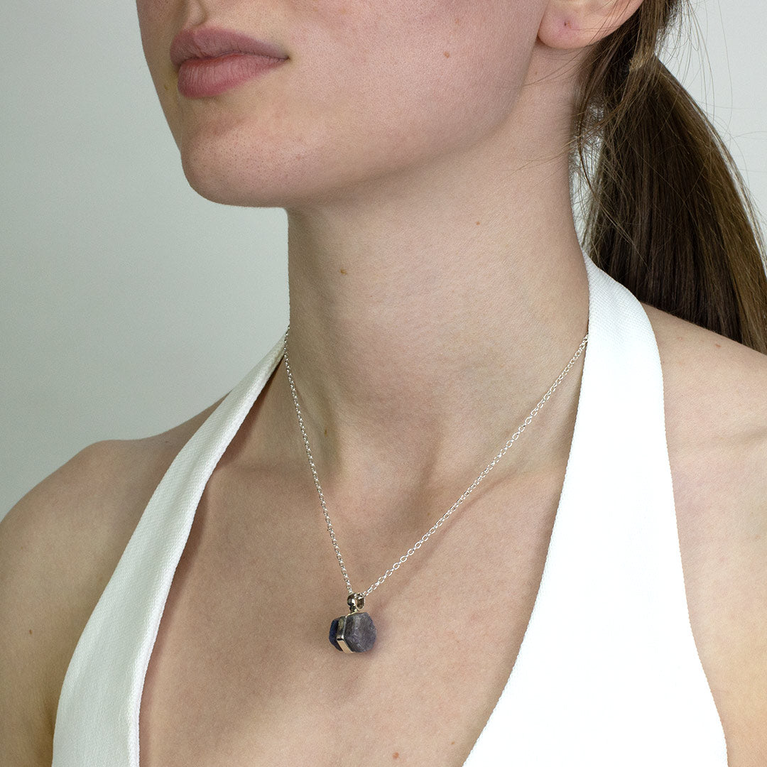 Woman wearing a silver necklace with a blue stone on a plain background