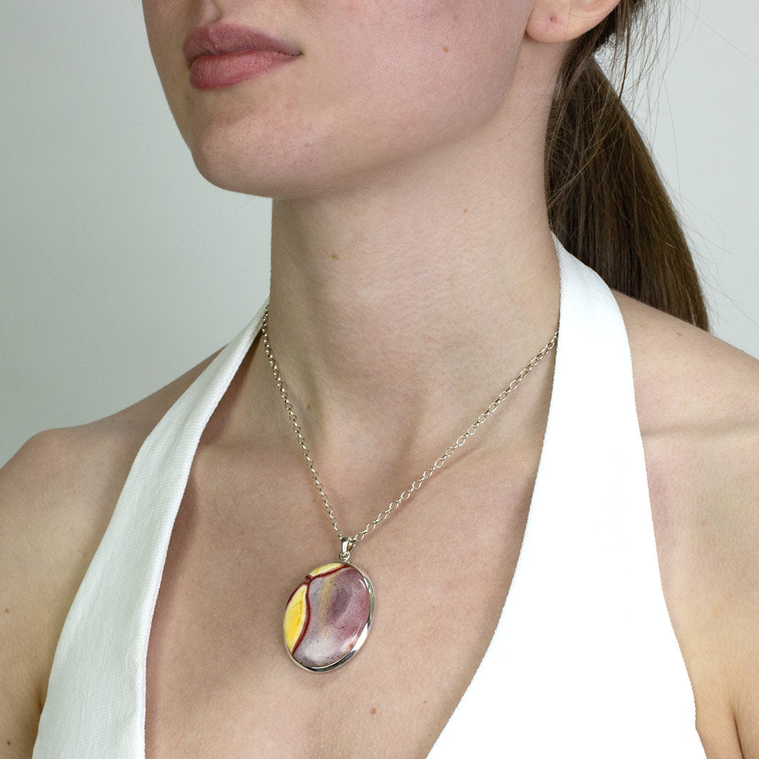 Woman wearing a silver necklace with a red and yellow stone on a plain background