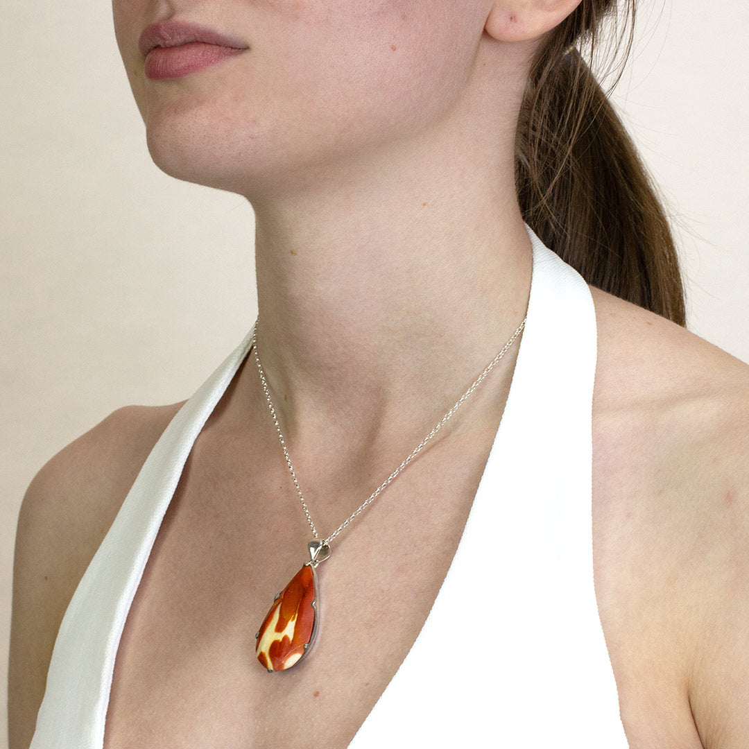 Woman wearing a silver necklace with a red and yellow stone on a plain background