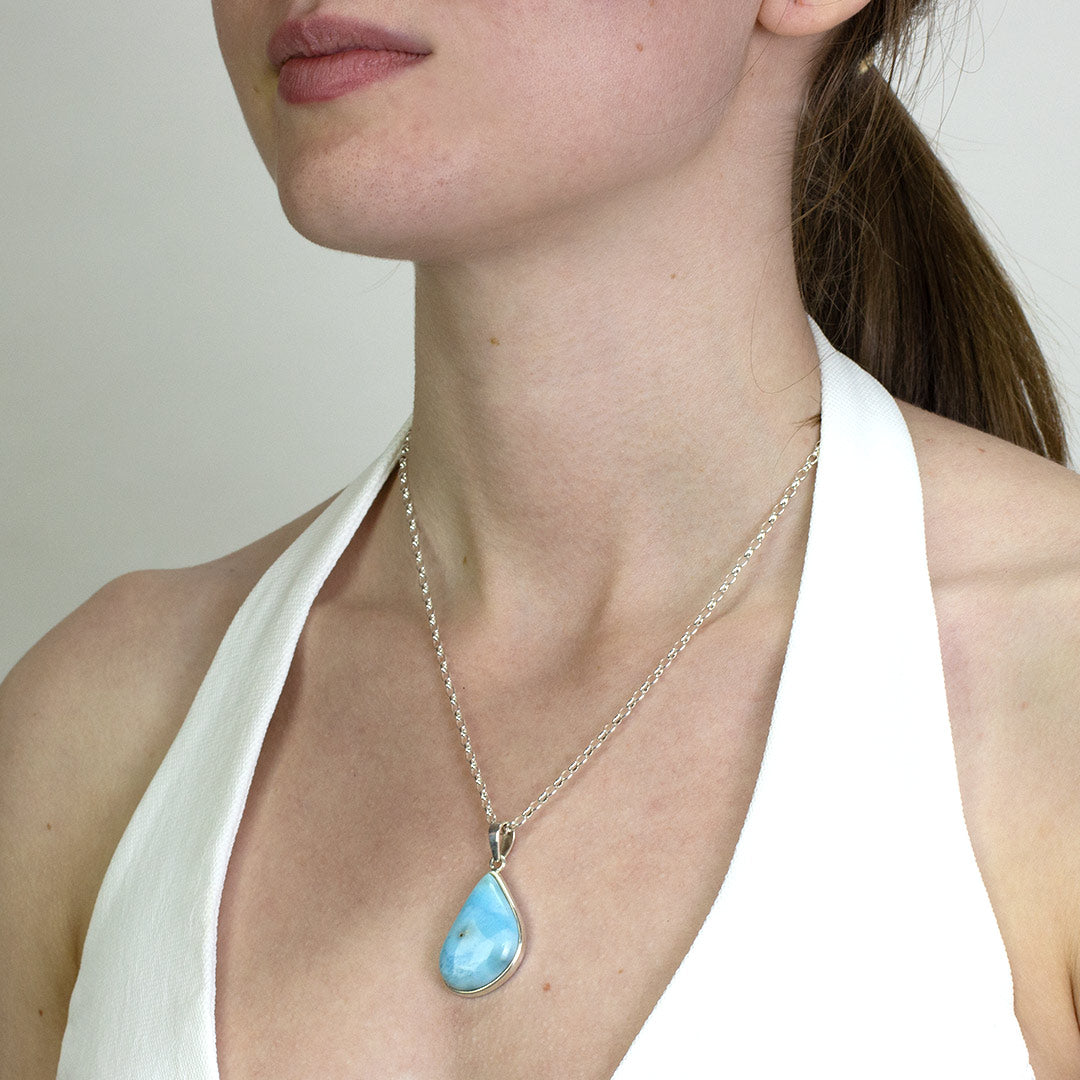 Woman wearing a silver necklace with a light blue and white stone on a plain background