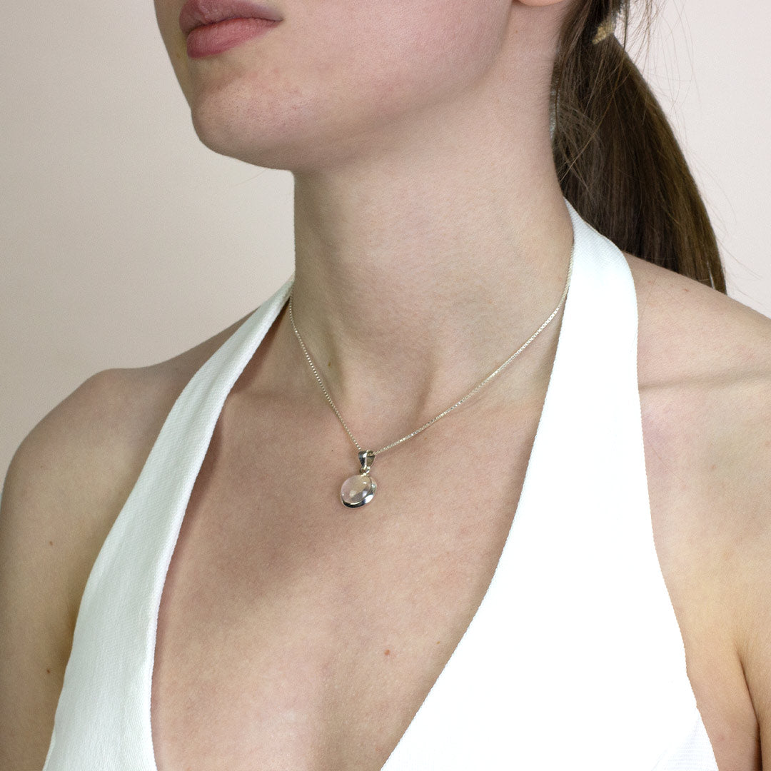 Woman wearing a silver necklace with a clear gemstone against a neutral background