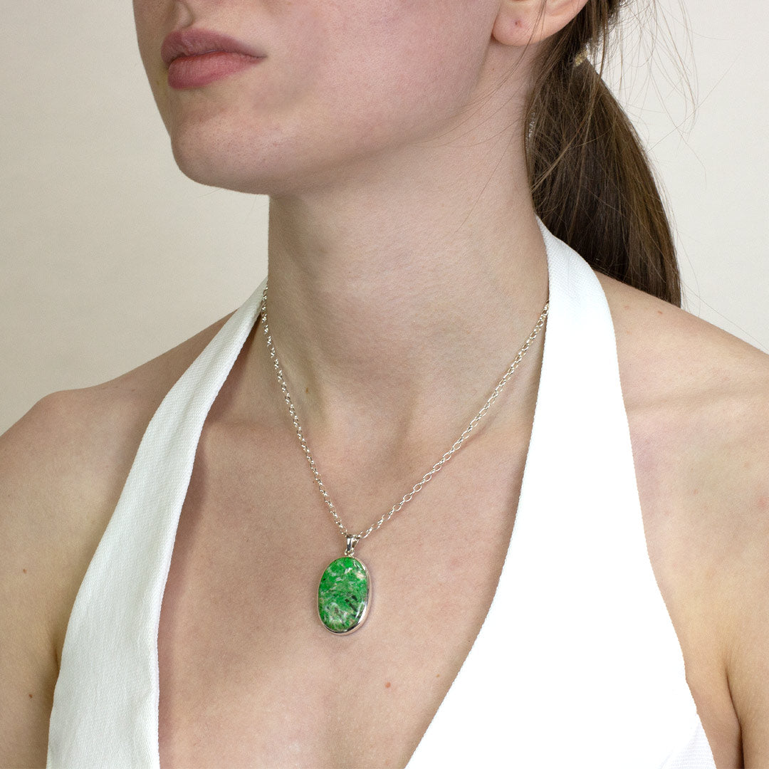 Woman wearing a silver necklace with a green gemstone on a plain background