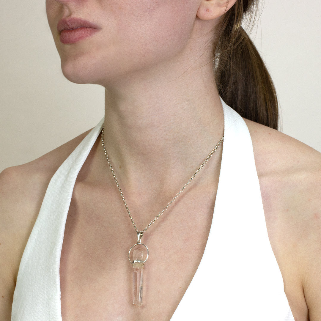 Woman wearing a silver necklace with a light pink stone on a plain background