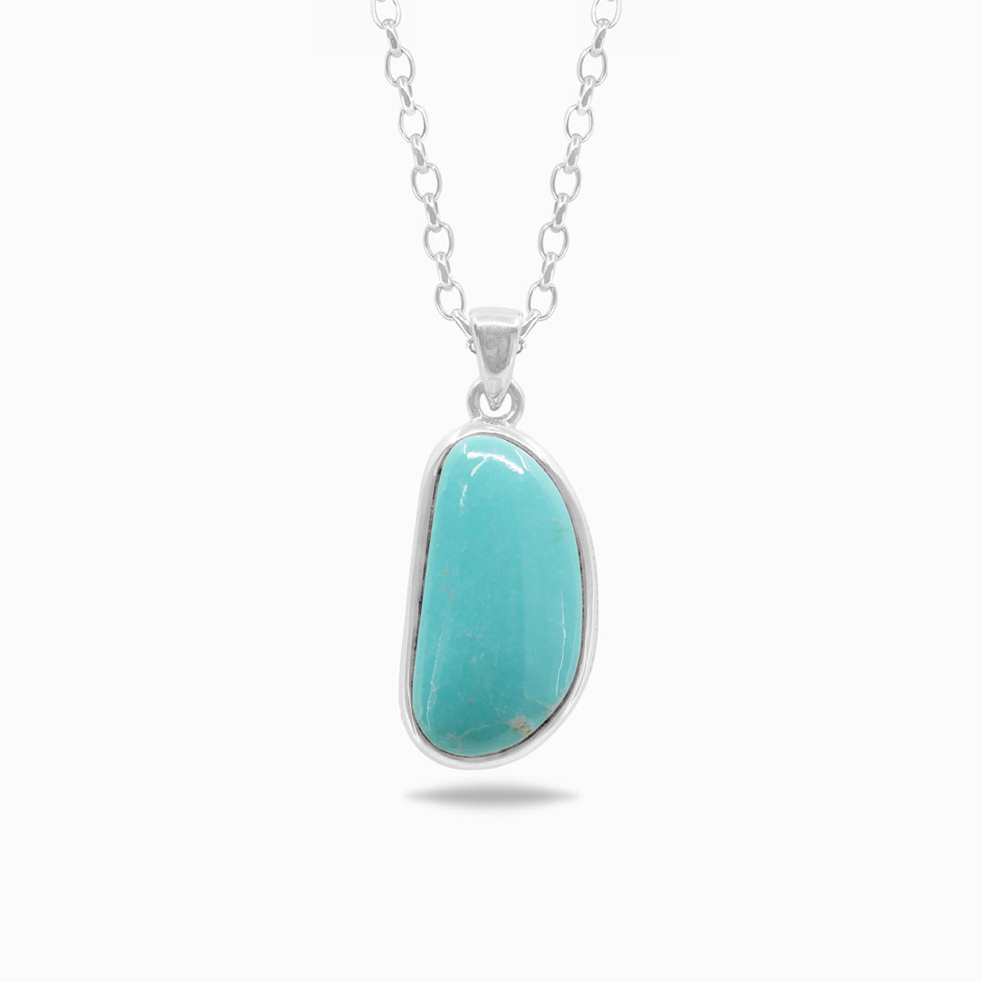 A silver necklace featuring a polished freeform turquoise stone, against a white background.