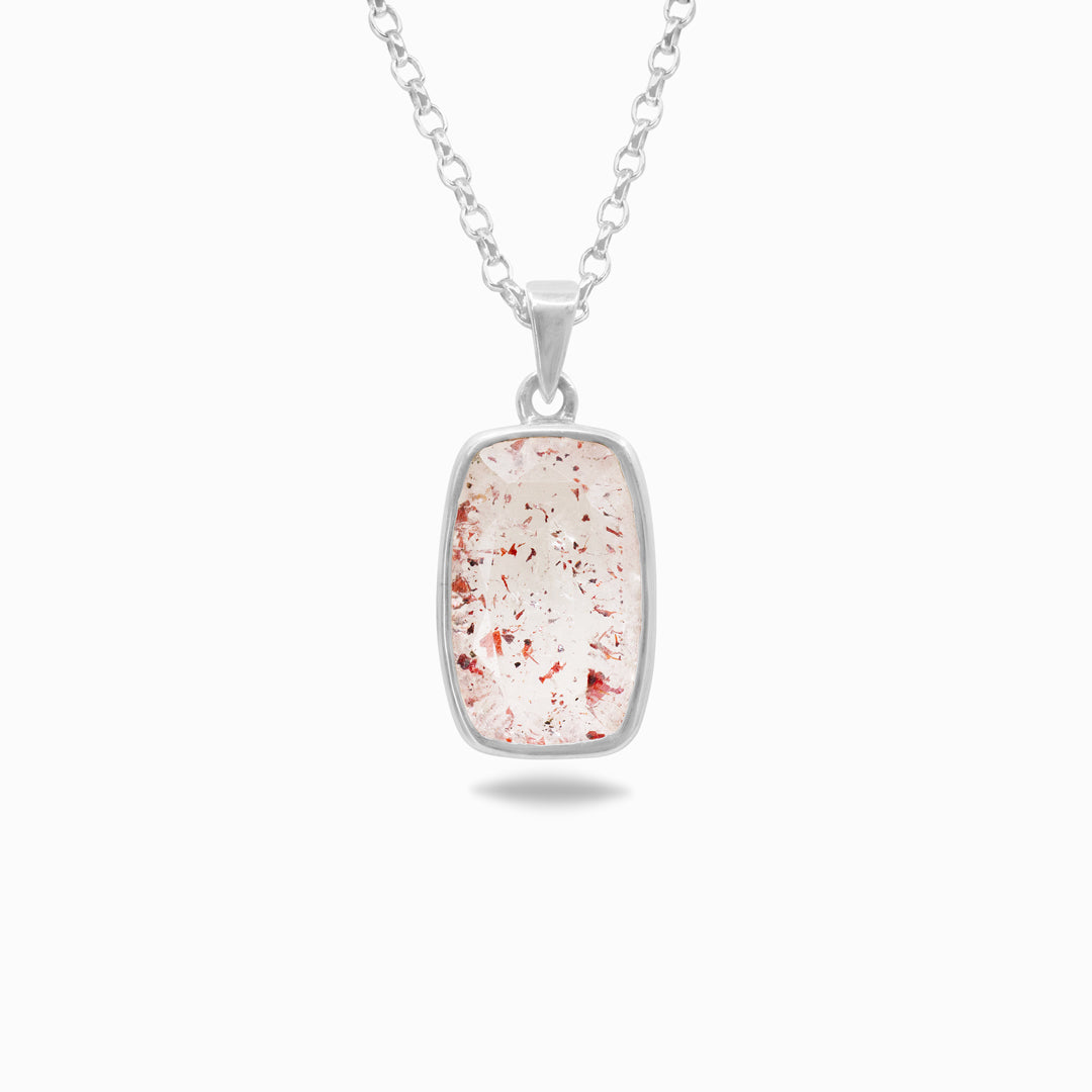 Silver necklace with a clear stone with pink and red inclusions on a white background
