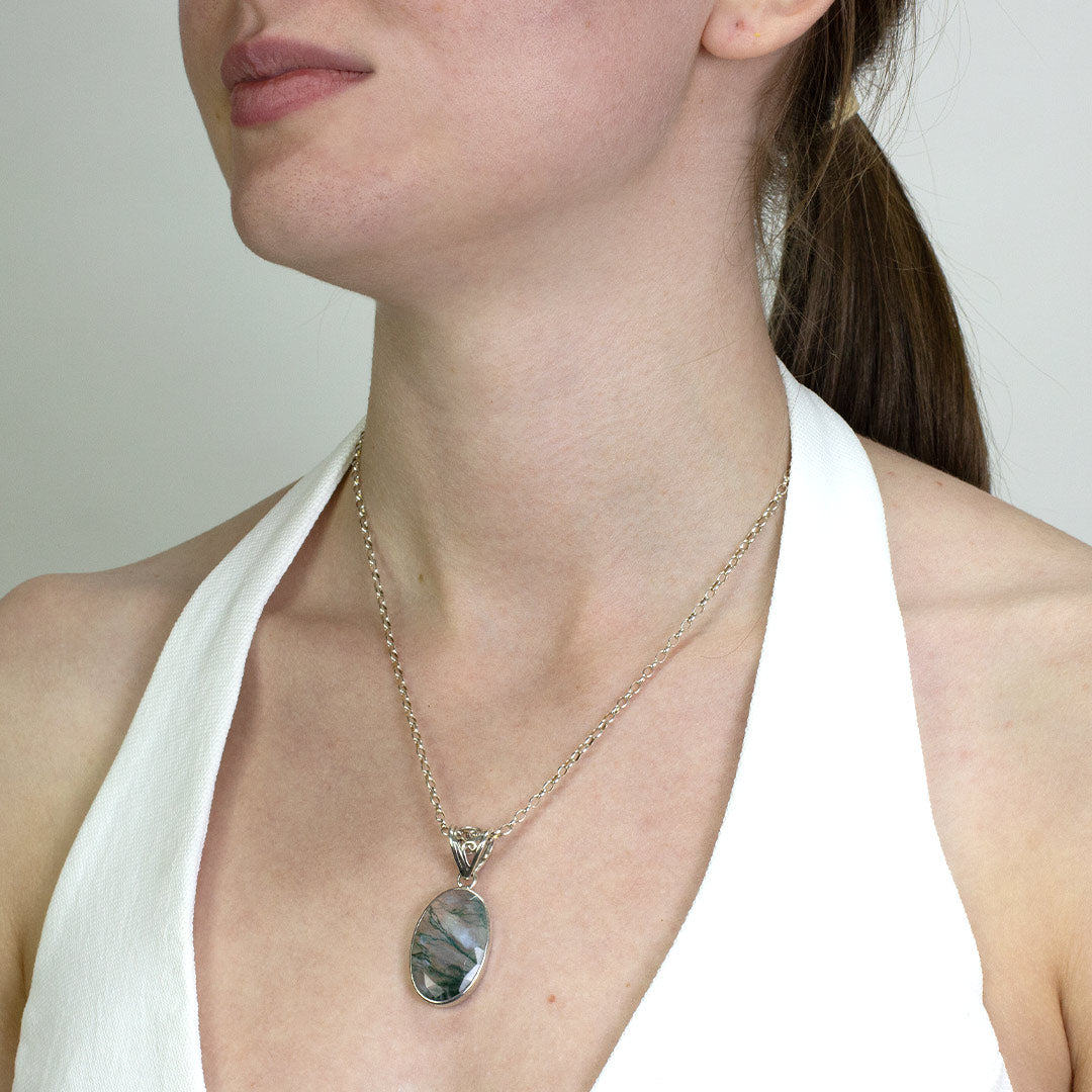 Woman wearing a silver necklace with translucent gemstone with green inclusions on a plain background