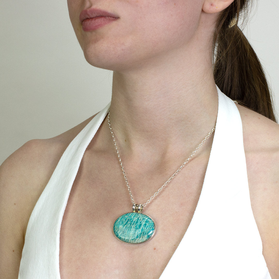 Woman wearing a silver necklace with a green and white stone on a plain background