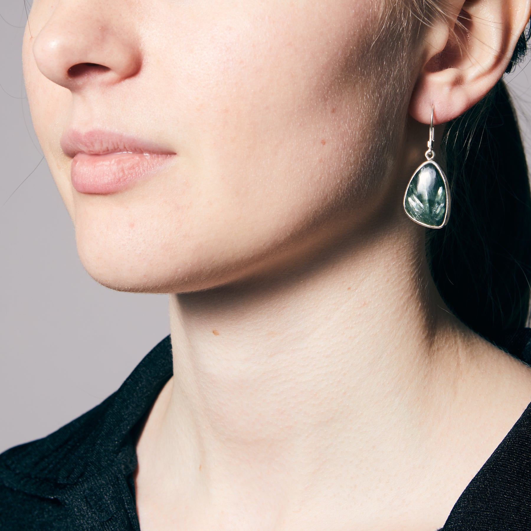 Close-up of a person wearing a green freeform earring against a neutral background