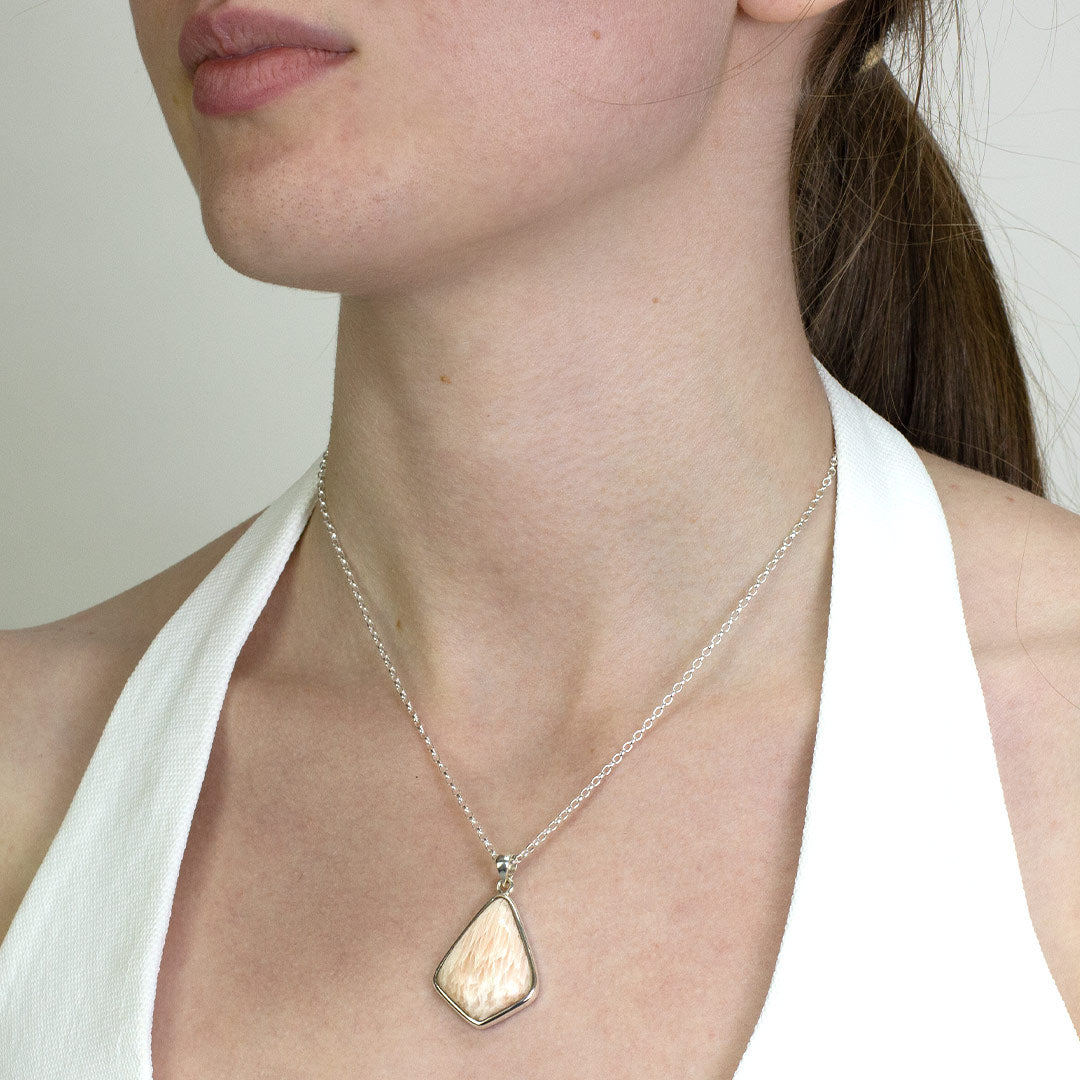 Woman wearing a silver necklace with a light pink gemstone on a plain background.
