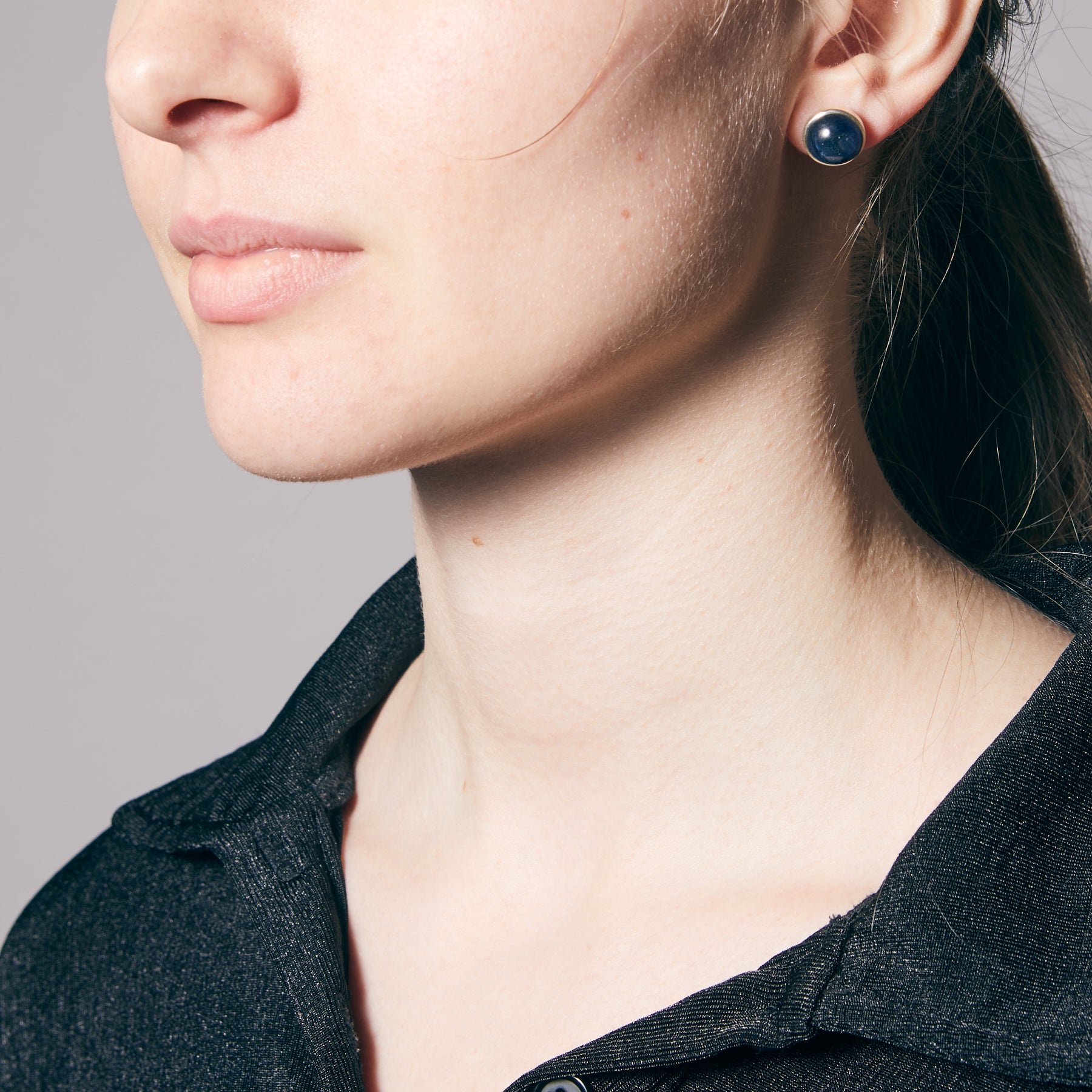 Close-up of a person wearing dark blue earrings against a neutral background