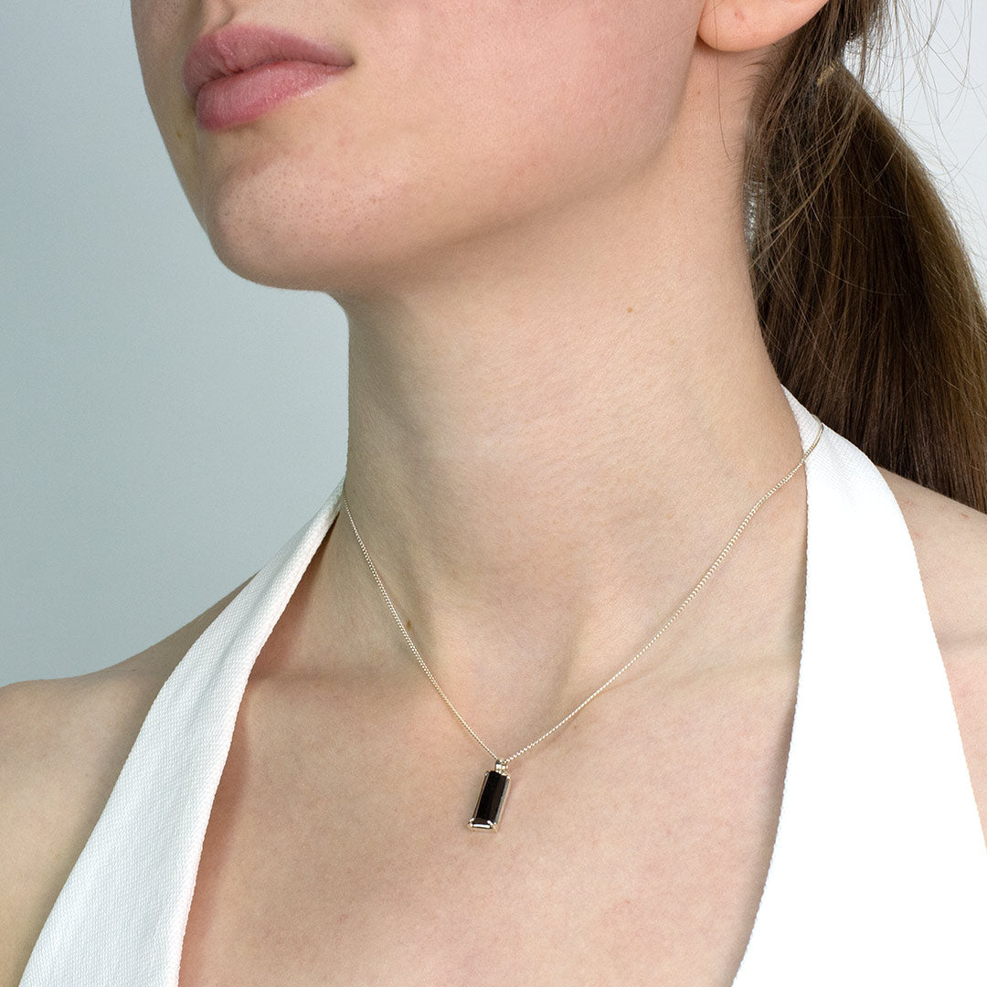 Woman wearing a silver necklace with a dark blue gemstone pendant on a plain background