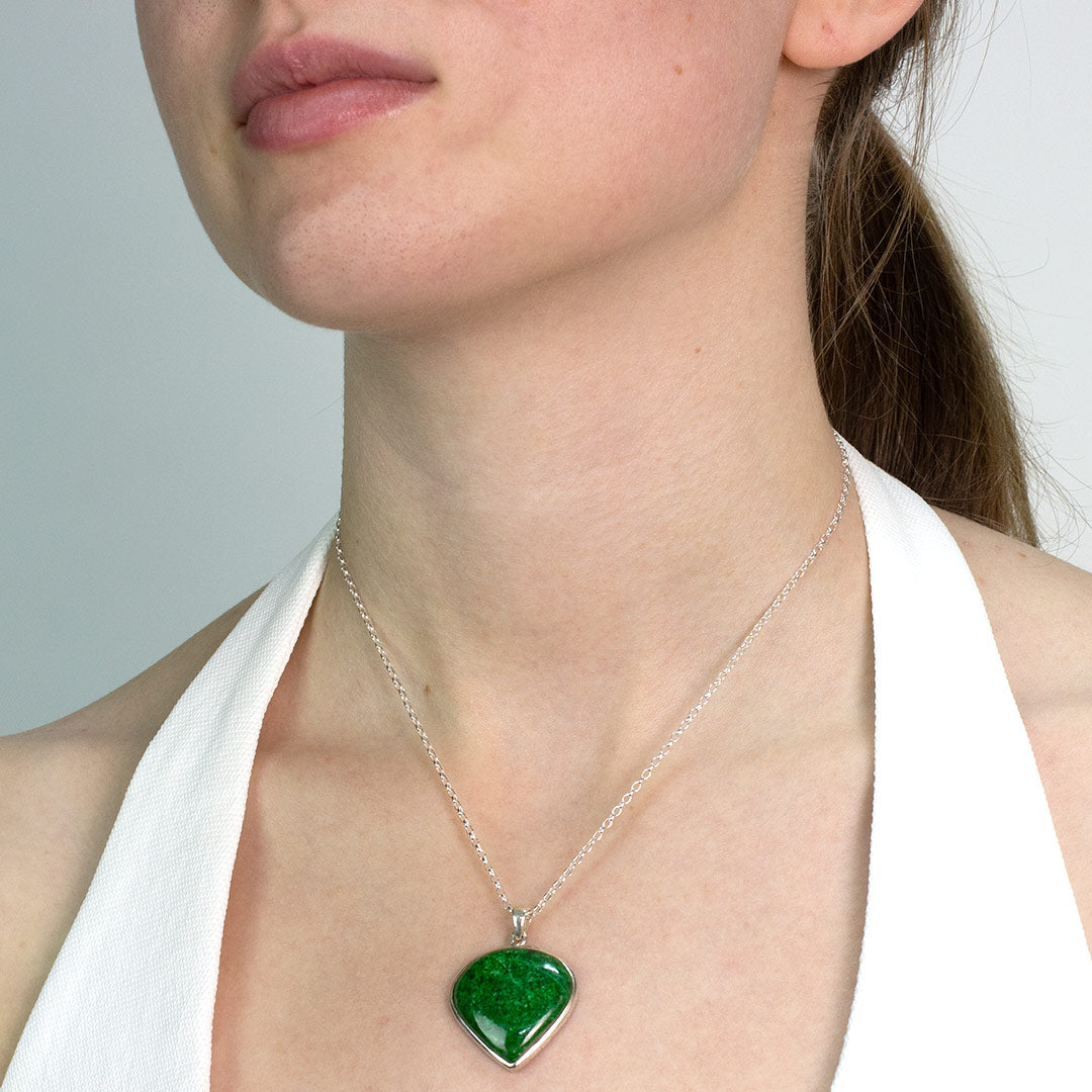 Woman wearing a silver necklace with a dark green gemstone on a plain background
