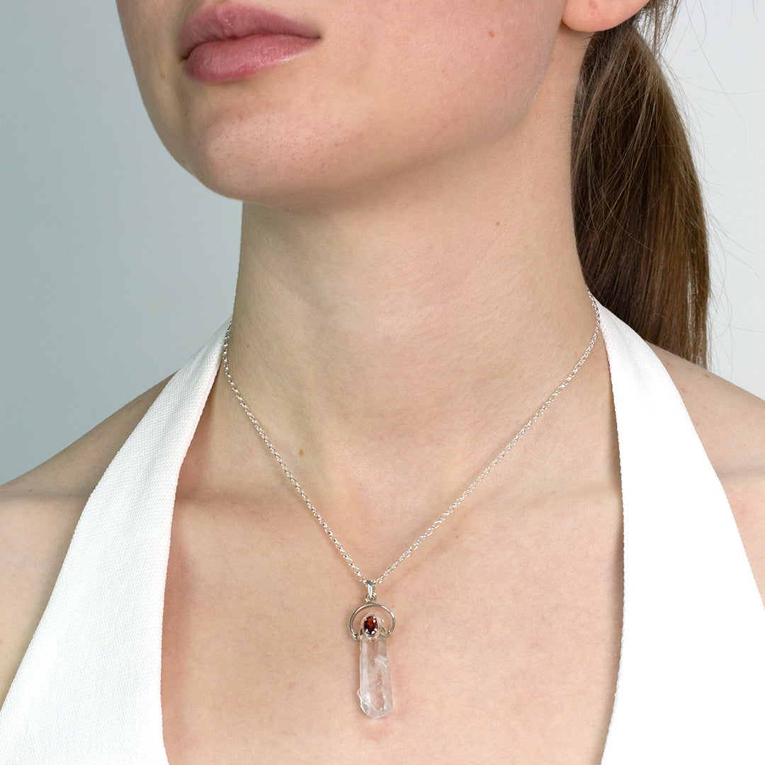 Woman wearing a silver necklace with a pendant featuring clear and red gemstones on a plain background