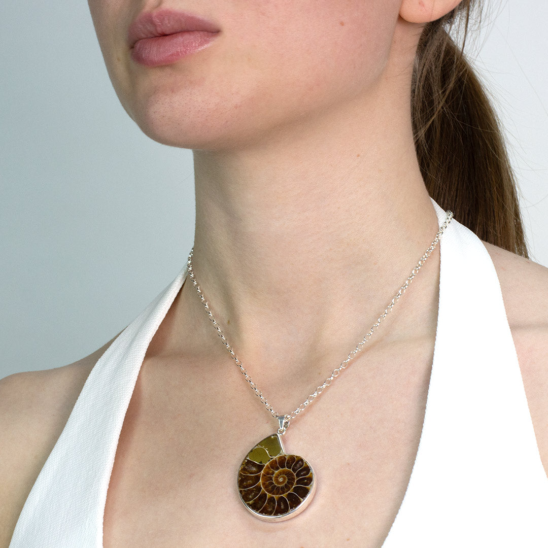 Woman wearing a Ammonite fossil pendant on a silver chain against a plain background