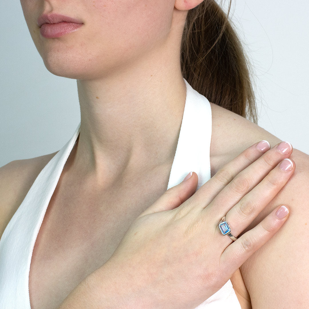Woman wearing a silver ring with a rectangular blue gemstone against a plain background