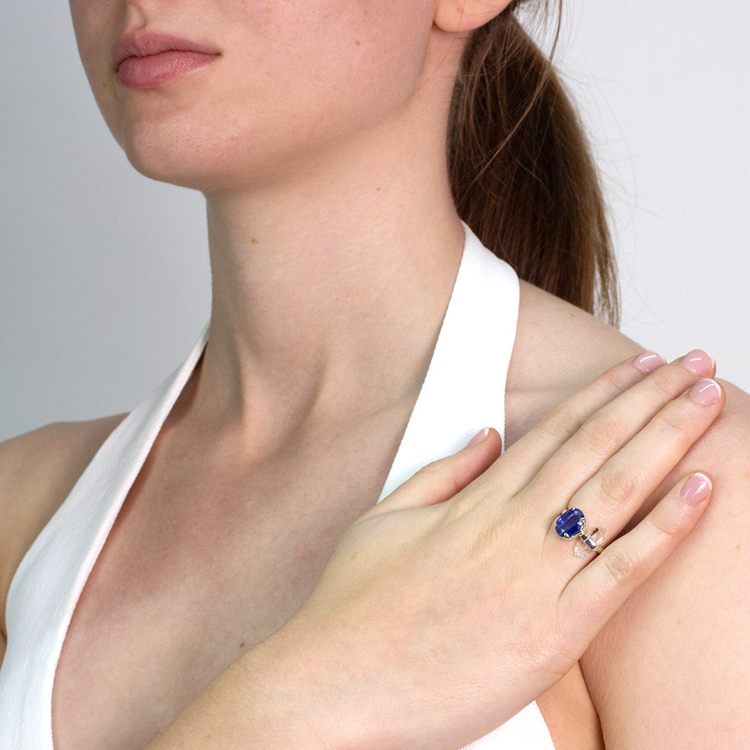 Woman wearing a silver ring with blue and clear gemstones against a plain background