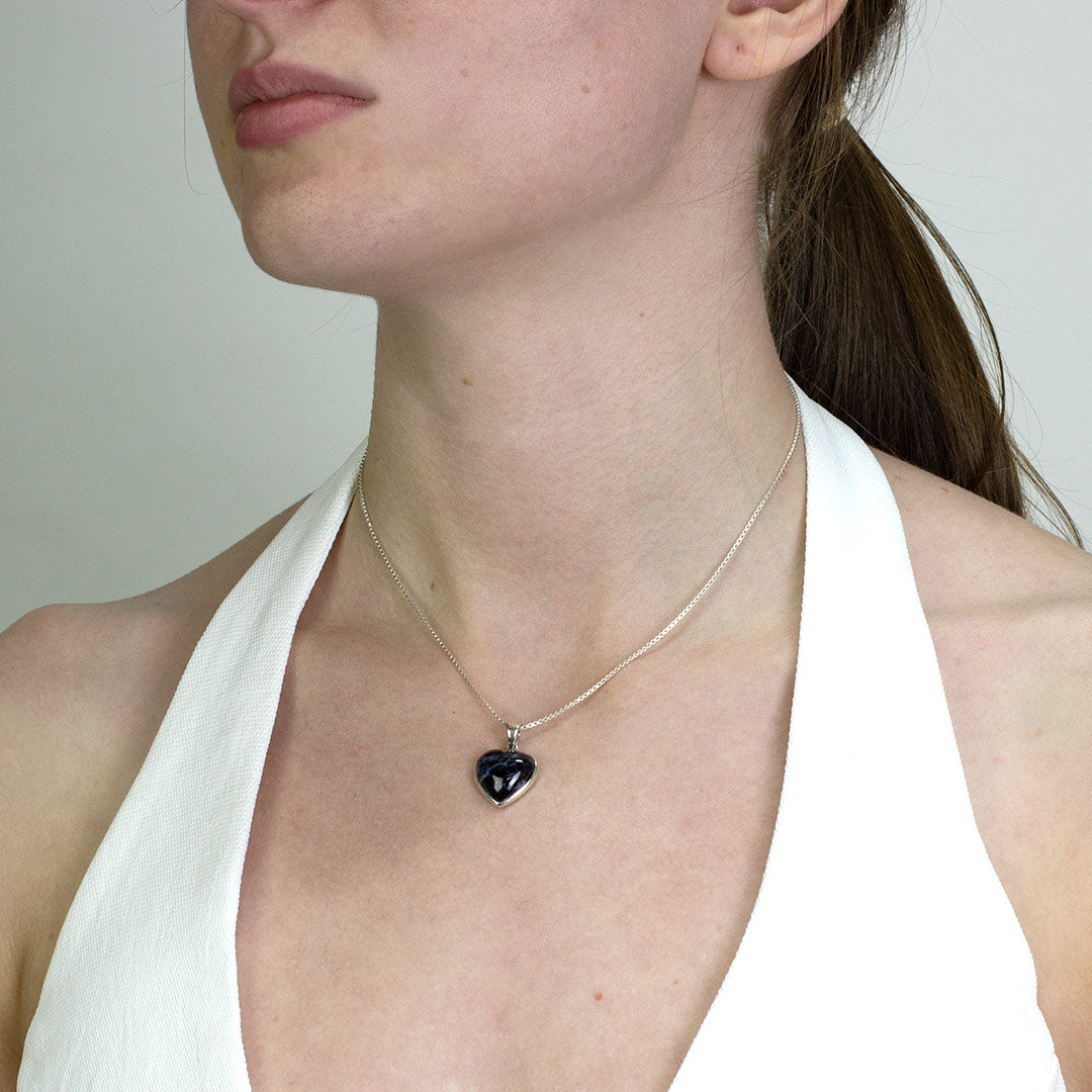 Woman wearing a necklace with a heart-shaped pendant on a plain background