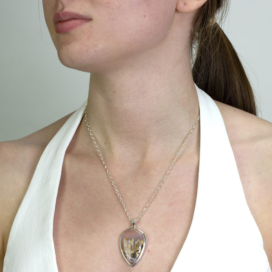 Woman wearing a silver necklace with a brown pendant on a plain background