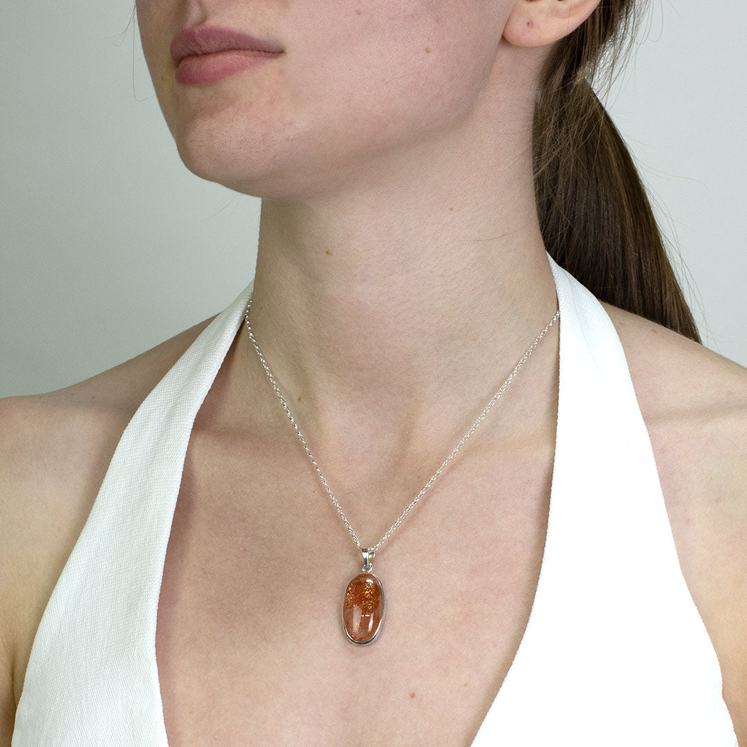 Woman wearing a silver necklace with an orange stone on a plain background