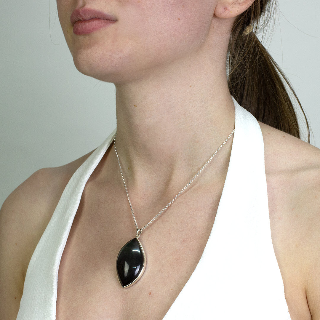Woman wearing a silver necklace with a black stone on a plain background
