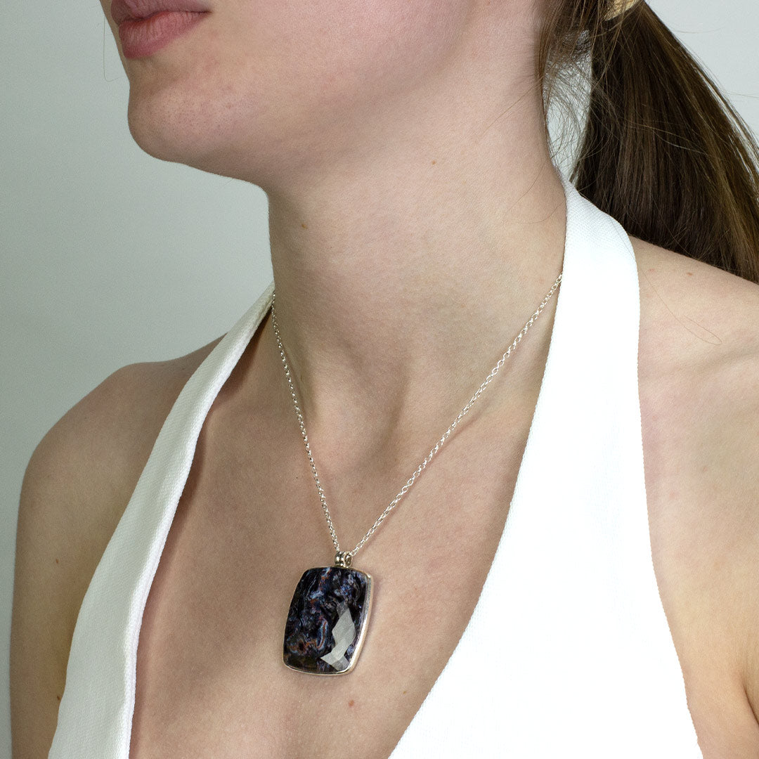 Woman wearing a silver necklace with a dark blue stone on a plain background.
