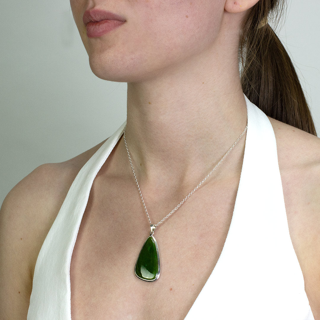 Woman wearing a silver necklace with a green stone on a plain background.