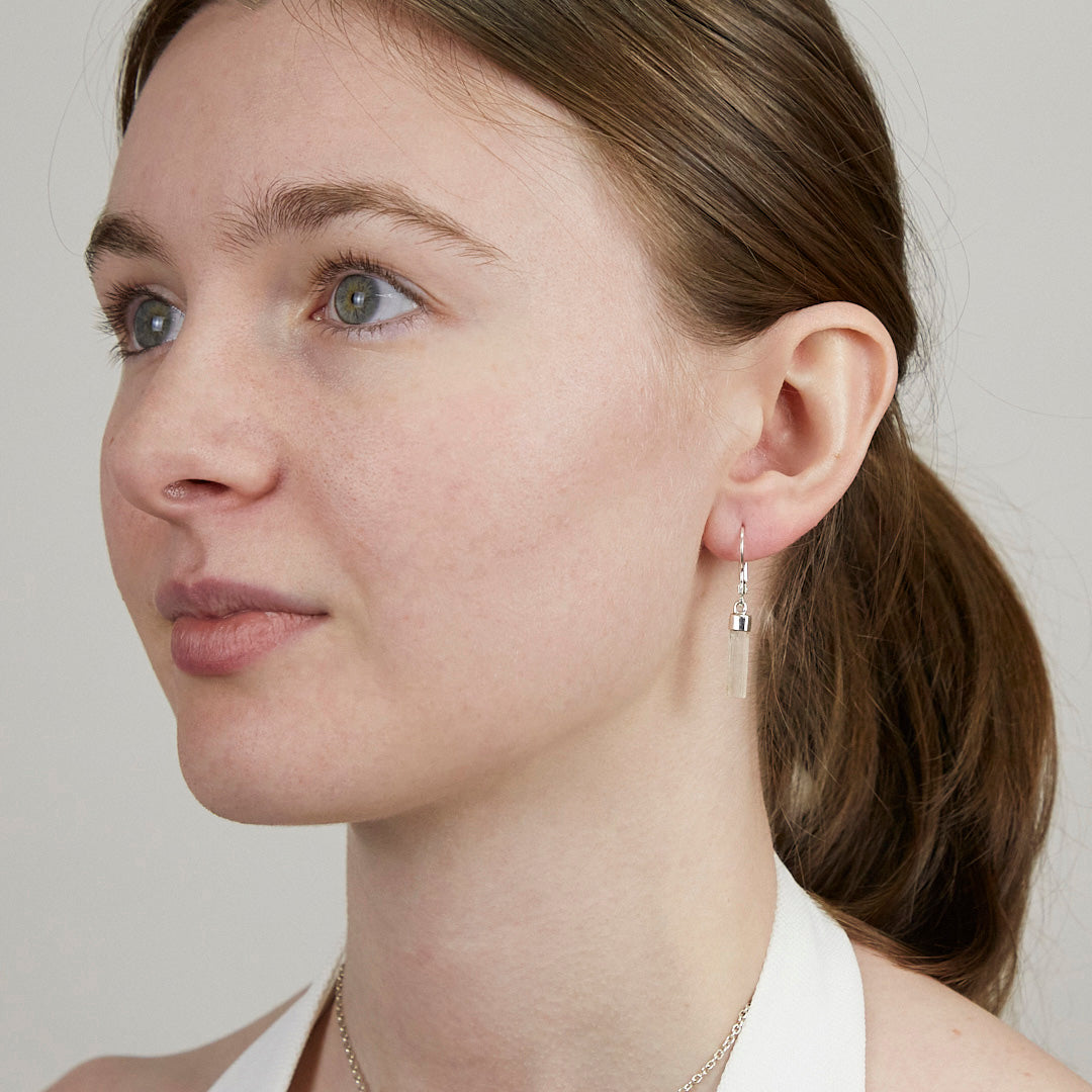 Close-up of a woman wearing silver earrings with clear stones on a plain background