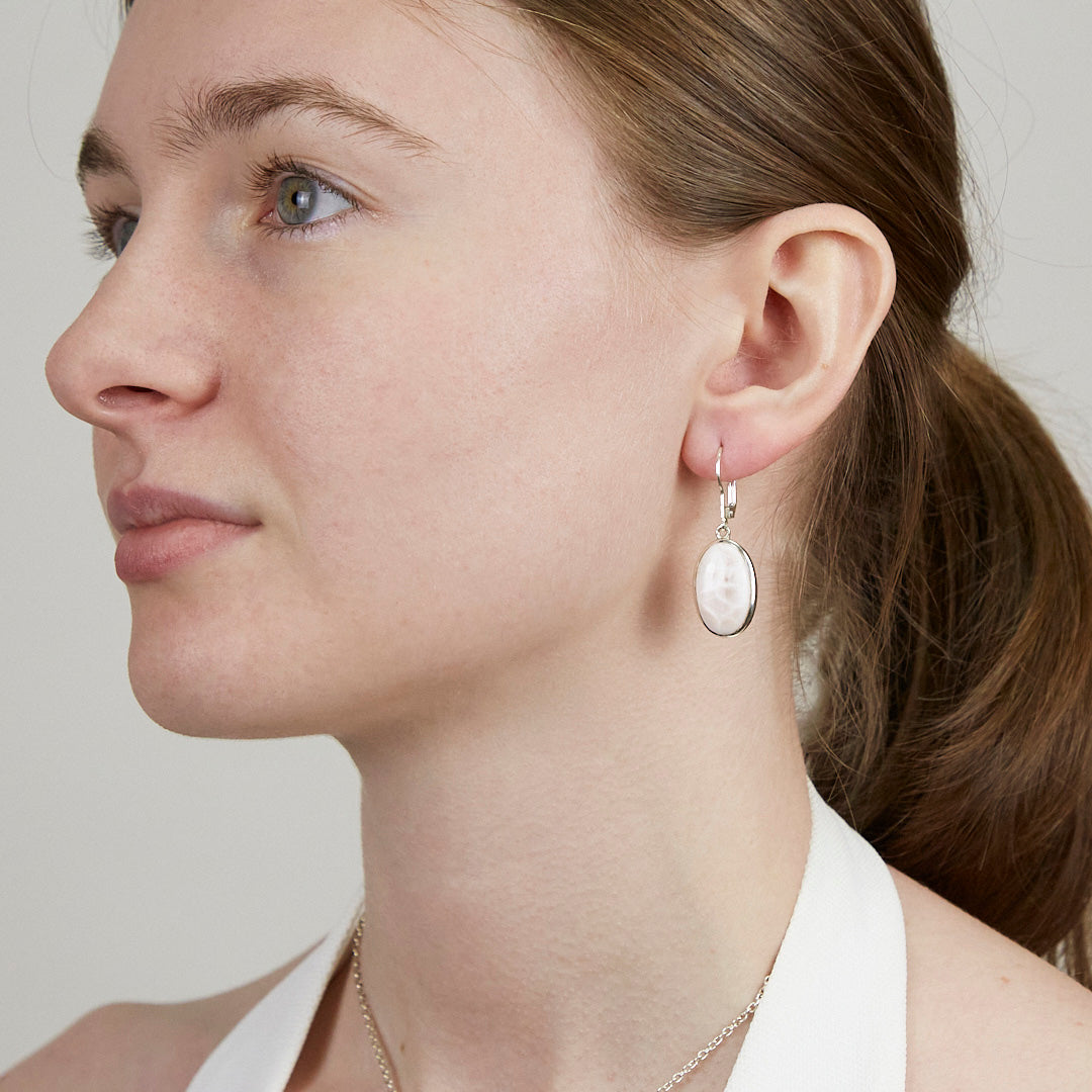 Close-up of a woman wearing a silver earring with white and pink gemstone on a white background